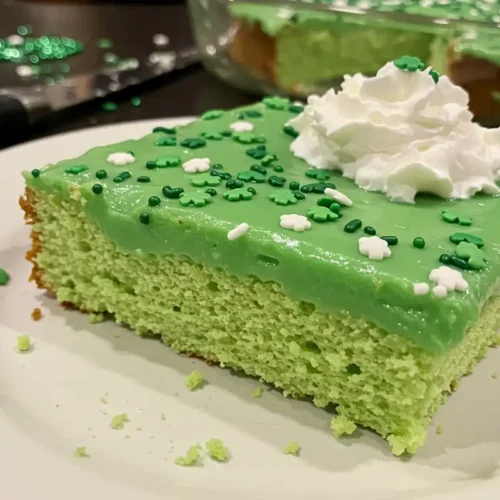 A slice of St. Patrick's Day Poke Cake shows the green pudding filling and sprinkles.