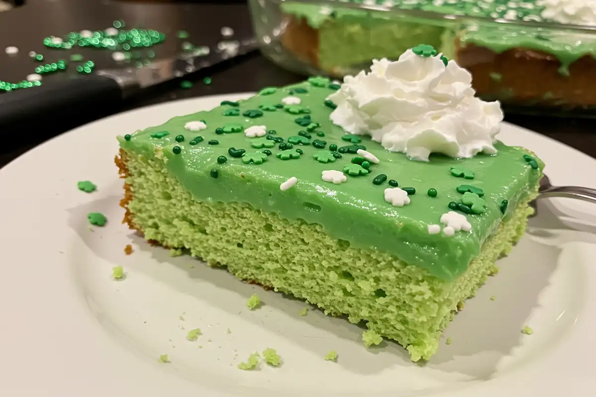A slice of St. Patrick's Day Poke Cake shows the green pudding filling and sprinkles.