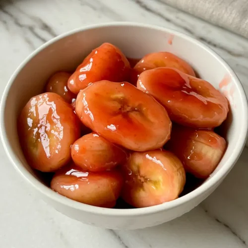 Close-up top-down view of the finished Bananas in Strawberry Sauce in a small bowl, showing banana slices coated in glossy red sauce.