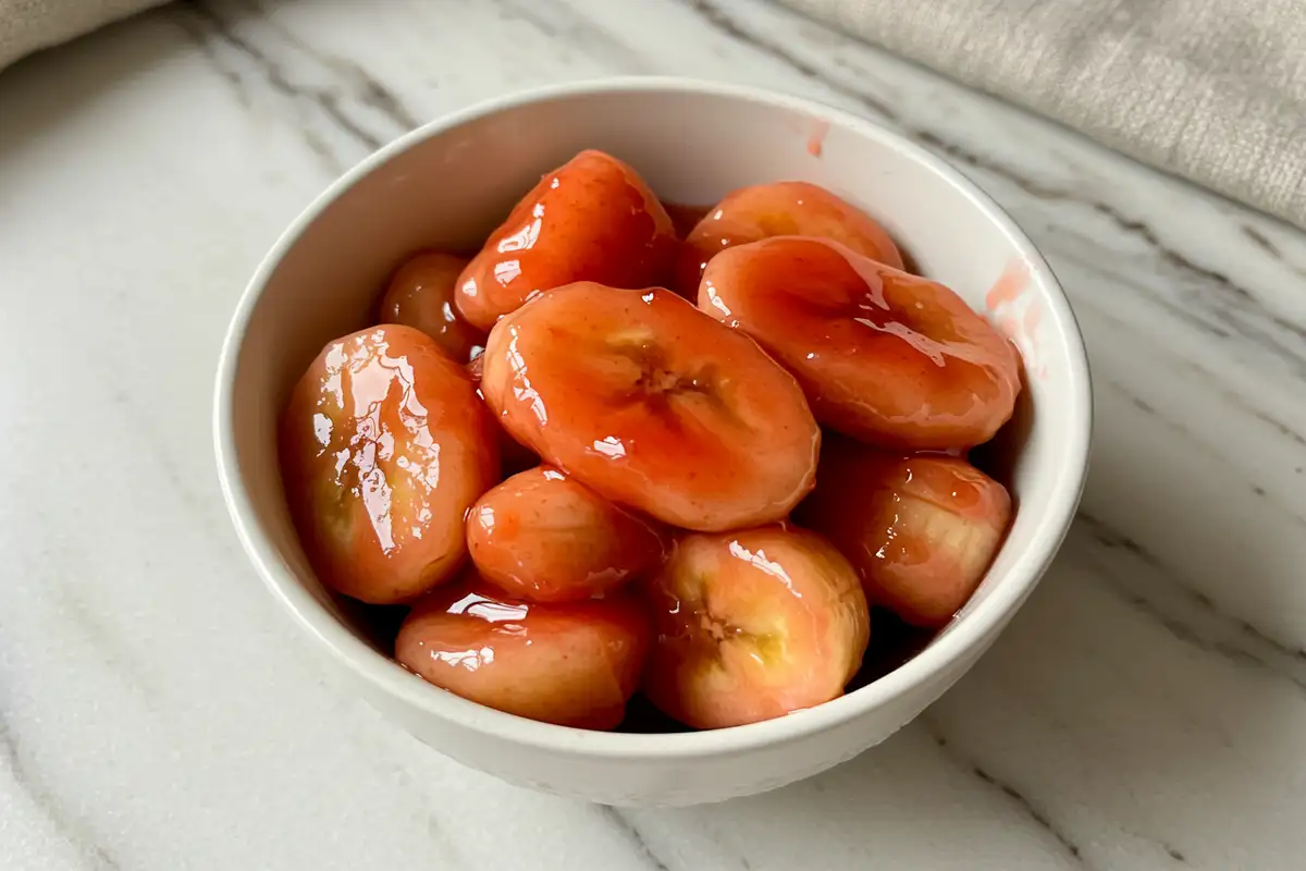 Close-up top-down view of the finished Bananas in Strawberry Sauce in a small bowl, showing banana slices coated in glossy red sauce.
