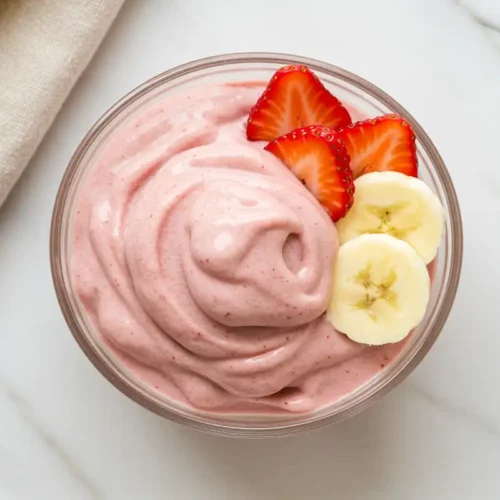 Close-up top-down view of the finished Strawberry Banana Nice Cream in a glass bowl, garnished with fresh strawberry and banana slices.