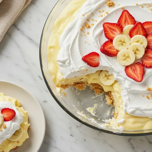 Close-up top-down view of finished strawberry banana pudding in a dish, garnished with whipped cream and fresh strawberries.