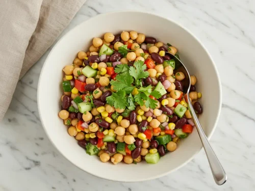 Close-up top-down view of a finished high-protein vegan dense bean salad in a serving bowl, garnished with fresh herbs.