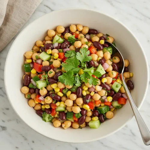 Close-up top-down view of a finished high-protein vegan dense bean salad in a serving bowl, garnished with fresh herbs.