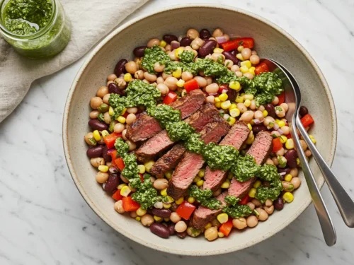 Top-down close-up of the finished steak chimichurri dense bean salad in a serving bowl, drizzled with chimichurri.