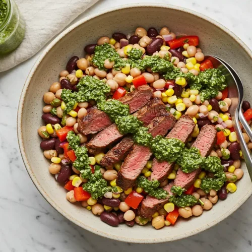 Top-down close-up of the finished steak chimichurri dense bean salad in a serving bowl, drizzled with chimichurri.
