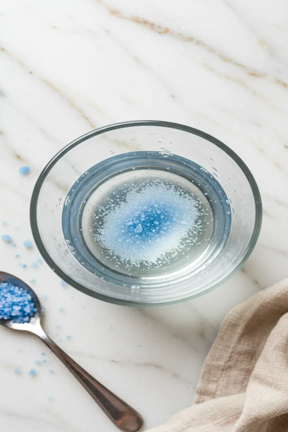 Close-up top-down view of Persian blue salt dissolving in a glass of water for the Blue Salt Trick Recipe, showing subtle shimmer and blue flecks, with a natural, home-mixed feel.