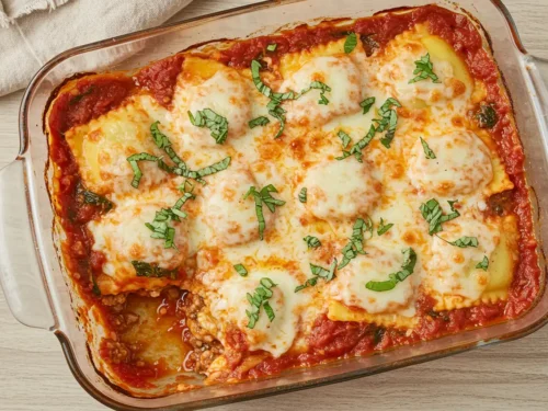 Close-up top-down view of the finished Baked Spinach Ravioli casserole in its 9x13 baking dish, showing bubbly sauce, golden melted cheese crust, garnished with fresh basil/parsley, looking natural and home-baked.