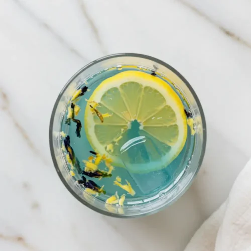 Close-up top-down view of the finished Brazilian Mounjaro inspired wellness drink in a clear glass, showing suspended ginger and its final color, looking natural, refreshing, and home-prepared on a light marble surface.