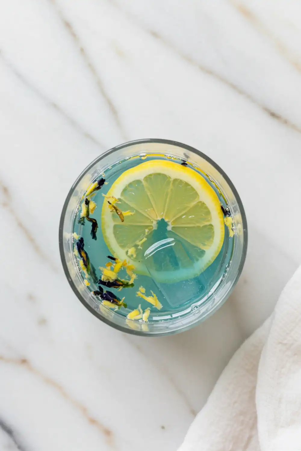 Close-up top-down view of the finished Brazilian Mounjaro inspired wellness drink in a clear glass, showing suspended ginger and its final color, looking natural, refreshing, and home-prepared on a light marble surface.