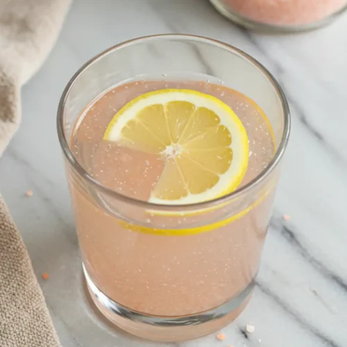 Close-up top-down view of the finished Pink Salt Trick Recipe drink in a glass, showing clear water with dissolved pink salt (and optional lemon slice), looking simple, natural, and home-prepared.