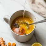 Close-up top-down view of the finished Pink Salt and Turmeric Morning Tonic in a sturdy mug with subtle wear, garnished with a lemon slice, looking natural and home-prepared.